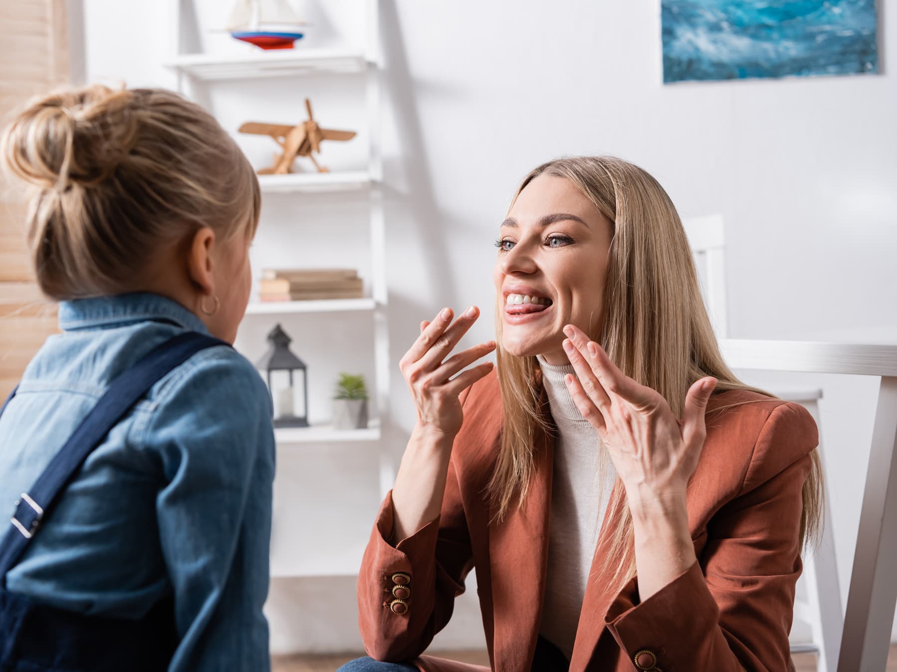 A speech language pathologist demonstrating a mouth shape to the person sitting opposite her.